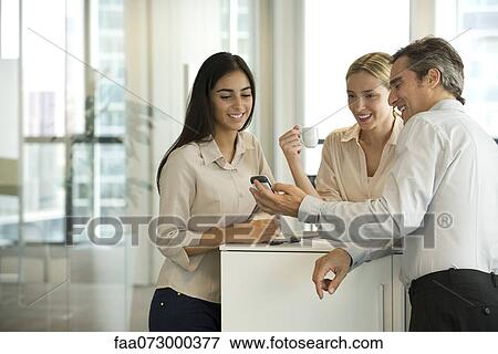 Colleagues looking at cell phone together during coffee break View Large Photo Image Stock Photo - Colleagues looking at cell phone together during coffee break. Fotosearch