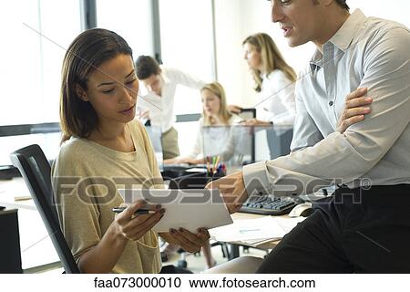 Colleagues looking at document together in office View Large Photo Image Stock Image - Colleagues looking at document together in office. Fotosearch