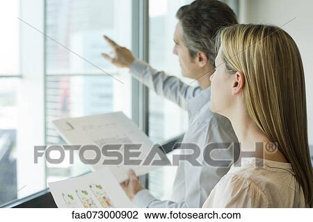 Colleagues looking holding blueprints and looking out window View Large Photo Image Stock Image - Colleagues looking holding blueprints and looking out window. Fotosearch