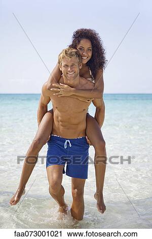 Stock Image - Couple at the beach, man carrying woman on his back. Fotosearch