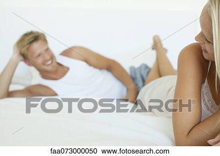 Stock Image - Couple lying on bed, woman smiling over her shoulder at man. Fotosearch