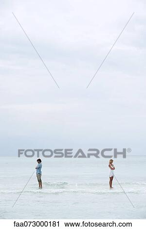 Stock Image - Couple standing apart in sea with backs turned toward each other. Fotosearch