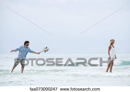 Couple standing in sea, woman walking away from man as he holds out a bouquet View Large Photo Image Stock Photo - Couple standing in sea, woman walking away from man as he holds out a bouquet. Fotosearch