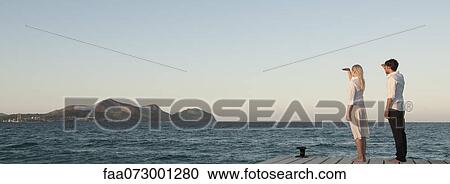 Stock Image - Couple standing on pier looking at view. Fotosearch