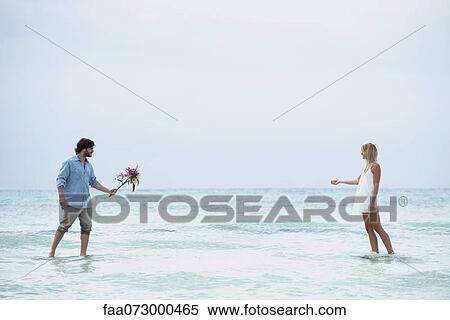Couple walking in sea towards each other, man holding out bouquet View Large Photo Image Stock Photography - Couple walking in sea towards each other, man holding out bouquet. Fotosearch
