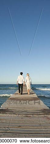Couple walking on pier holding hands, rear view View Large Photo Image Stock Image - Couple walking on pier holding hands, rear view. Fotosearch