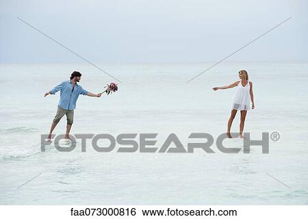 Stock Photograph - Couple walking on water towards each other, man holding out bouquet. Fotosearch