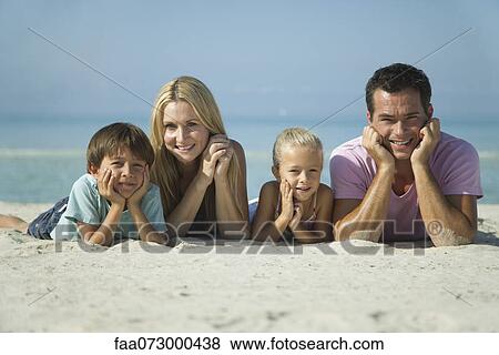 Stock Photo - Family lying on sand at the beach, portrait. Fotosearch