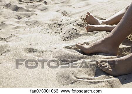 Stock Image - Feet on sandy beach, low section. Fotosearch