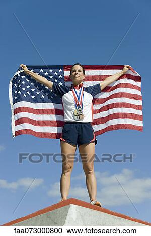Stock Image - Female athlete being honored on podium, holding up American flag. Fotosearch