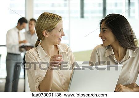 Female colleagues chatting in office View Large Photo Image Stock Photograph - Female colleagues chatting in office. Fotosearch