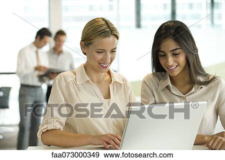 Stock Photo - Female colleagues working together on laptop computer. Fotosearch
