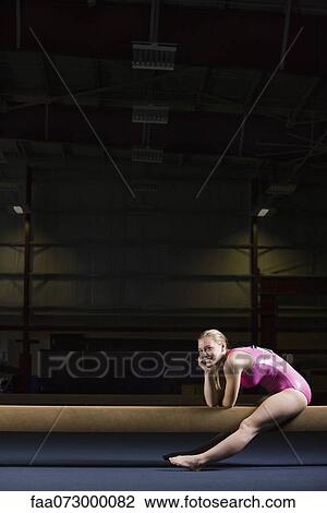 Stock Image - Female gymnast sitting on balance beam. Fotosearch