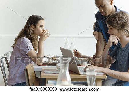 Stock Image - Friends in restaurant, woman dining, man using laptop computer. Fotosearch