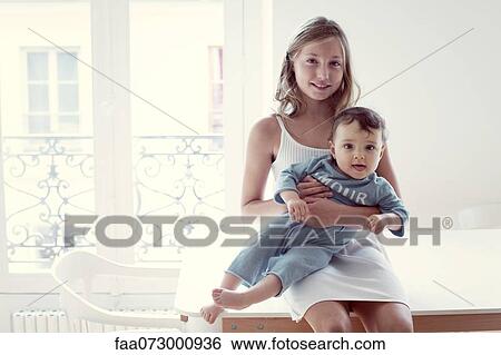 Stock Photograph - Girl holding baby sister on lap, portrait. Fotosearch