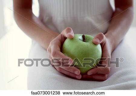 Stock Photo - Girl holding green apple, mid section. Fotosearch
