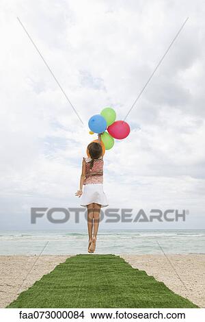 Girl jumping with bunch of balloons, reaching for sky, rear view View Large Photo Image Picture - Girl jumping with bunch of balloons, reaching for sky, rear view. Fotosearch
