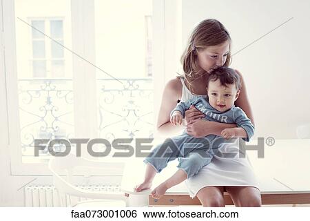 Stock Photograph - Girl kissing baby sister on lap, portrait. Fotosearch