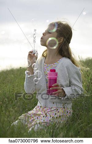 Girl kneeling in field, blowing bubbles View Large Photo Image Stock Photograph - Girl kneeling in field, blowing bubbles. Fotosearch