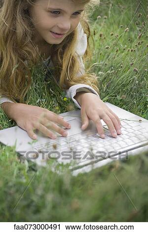 Girl lying in grass, using laptop computer View Large Photo Image Stock Image - Girl lying in grass, using laptop computer. Fotosearch