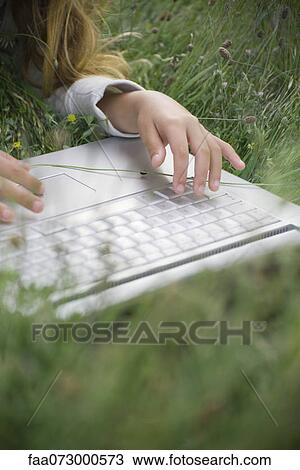 Girl lying in grass, using laptop computer View Large Photo Image Stock Image - Girl lying in grass, using laptop computer. Fotosearch