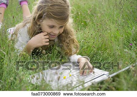 Stock Photo - Girl lying in grass, using laptop computer. Fotosearch