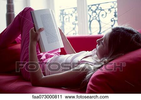 Stock Image - Girl reading book on couch. Fotosearch