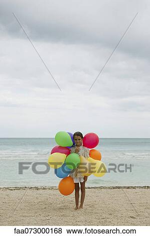 Stock Photo - Girl with bunch of colorful balloons on beach. Fotosearch