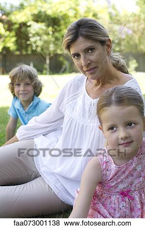 Stock Photo - Grandmother with grandchildren sitting on grass. Fotosearch