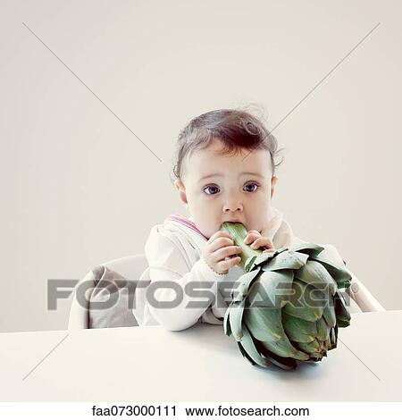 Stock Image - Infant biting fresh artichoke. Fotosearch