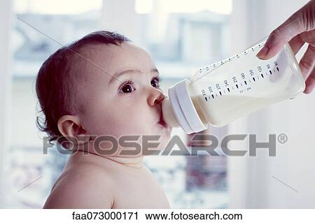 Stock Image - Infant drinking milk from baby bottle. Fotosearch