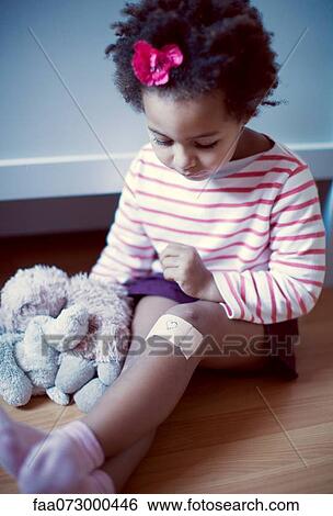 Stock Photograph - Little girl looking at adhesive bandage on knee. Fotosearch