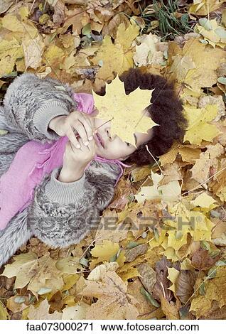 Stock Image - Little girl lying on bed of autumn leaves. Fotosearch