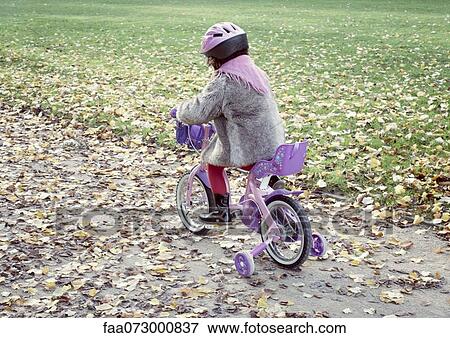 Stock Photo - Little girl riding bicycle in autumn landscape, rear view. Fotosearch