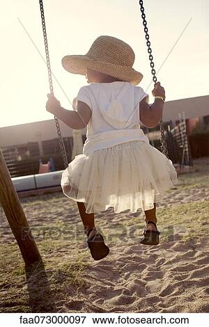 Stock Photo - Little girl sitting on swing, rear view. Fotosearch