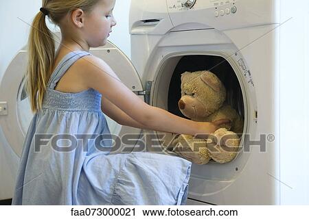 Stock Image - Little girl taking teddy bear out of dryer. Fotosearch