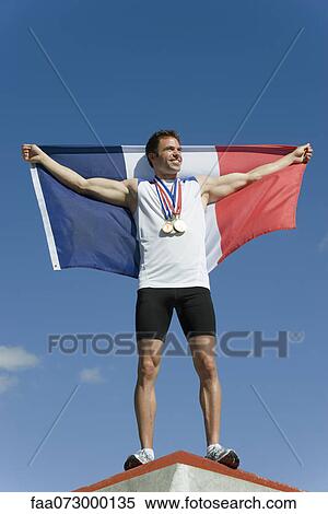 Stock Photography - Male athlete being honored on podium, holding up French flag. Fotosearch