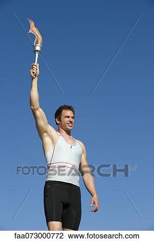 Stock Image - Male athlete holding up torch. Fotosearch