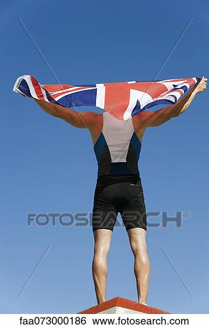 Male athlete on podium, holding up British flag, rear view View Large Photo Image Stock Photograph - Male athlete on podium, holding up British flag, rear view. Fotosearch