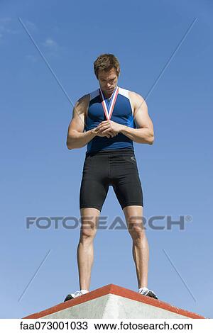 Male athlete on winner's podium, holding medal and looking down View Large Photo Image Stock Image - Male athlete on winner's podium, holding medal and looking down. Fotosearch