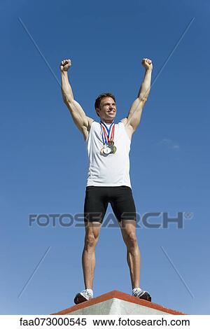 Male athlete standing on winner's podium with arms raised in victory View Large Photo Image Stock Photography - Male athlete standing on winner's podium with arms raised in victory. Fotosearch