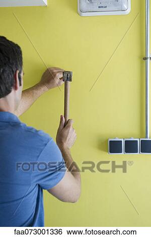 Stock Photograph - Man hammering nail into wall, rear view. Fotosearch