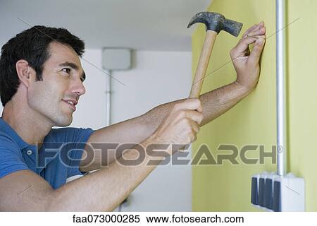 Man hammering nail into wall View Large Photo Image Stock Photography - Man hammering nail into wall. Fotosearch
