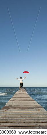 Man jumping on pier with umbrella, rear view View Large Photo Image Stock Photo - Man jumping on pier with umbrella, rear view. Fotosearch