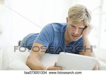 Man lying on stomach looking at digital tablet View Large Photo Image Picture - Man lying on stomach looking at digital tablet. Fotosearch
