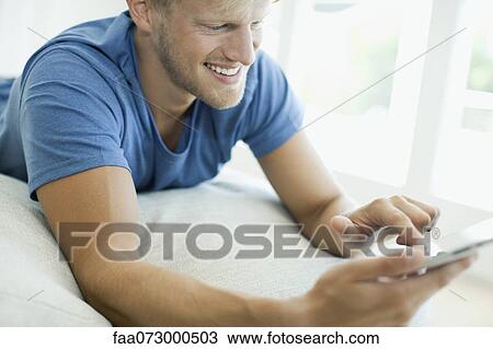 Stock Image - Man lying on stomach looking at digital tablet. Fotosearch