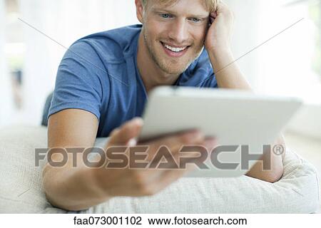 Man lying on stomach looking at digital tablet View Large Photo Image Stock Image - Man lying on stomach looking at digital tablet. Fotosearch