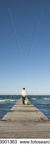Man pulling luggage walking towards end of pier View Large Photo Image Stock Image - Man pulling luggage walking towards end of pier. Fotosearch