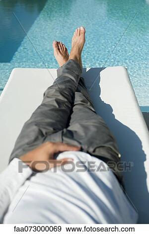 Stock Photo - Man relaxing on lounge chair beside pool. Fotosearch