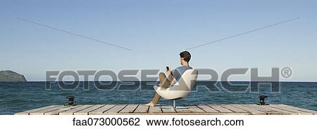 Man siitng in chair on dock using cell phone, rear view View Large Photo Image Stock Image - Man siitng in chair on dock using cell phone, rear view. Fotosearch